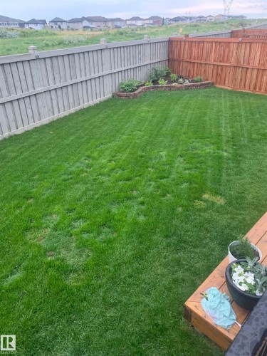 The property features a well-maintained lawn, a wooden fence, and a raised garden bed with various plants - 7490 Creighton Place, Edmonton, AB - Outdoor