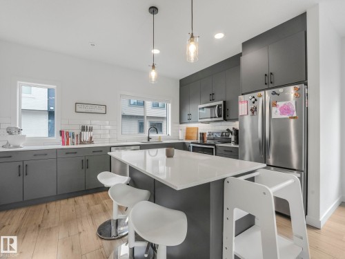 The kitchen features light wood flooring, grey cabinetry with dark hardware, white countertops, a white subway tile backsplash, and stainless steel appliances - 95 1010 Rabbit Hill Road, Edmonton, AB - Indoor Photo Showing Kitchen With Upgraded Kitchen