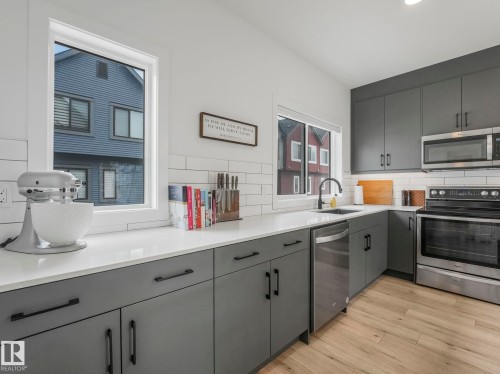 The kitchen features grey cabinetry, stainless steel appliances, and a white subway tile backsplash, all complemented by light wood-style flooring - 95 1010 Rabbit Hill Road, Edmonton, AB - Indoor Photo Showing Kitchen