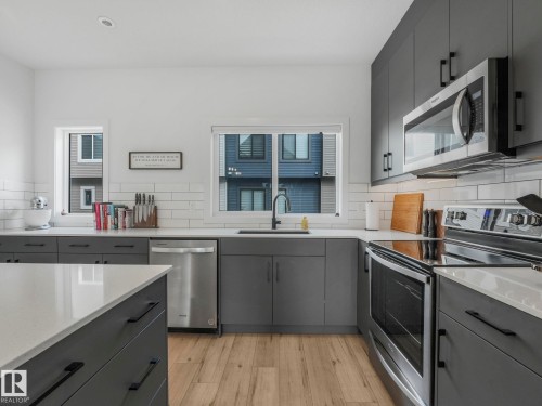 Modern kitchen featuring dark grey cabinetry, white countertops, stainless steel appliances, and light wood flooring - 95 1010 Rabbit Hill Road, Edmonton, AB - Indoor Photo Showing Kitchen
