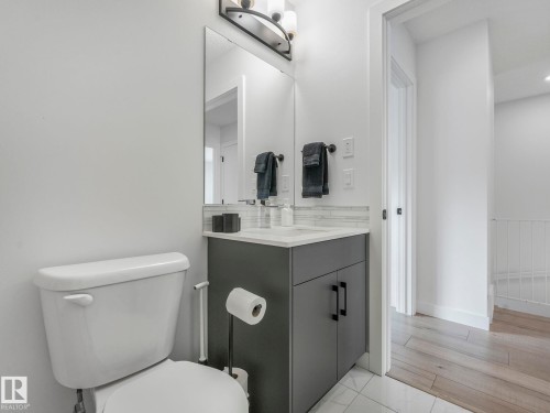 Bathroom featuring a white toilet, a vanity with a dark grey cabinet and white countertop, a mirror, and a wall-mounted light fixture - 95 1010 Rabbit Hill Road, Edmonton, AB - Indoor Photo Showing Bathroom