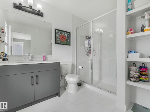 This bathroom features a contemporary gray vanity with a white countertop, a spacious walk-in shower with a glass enclosure, and built-in shelving providing additional storage - 95 1010 Rabbit Hill Road, Edmonton, AB - Indoor Photo Showing Bathroom
