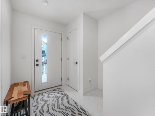 Inviting entryway featuring a white front door with a vertical window pane, tiled flooring, and a white staircase with a prominent handrail - 95 1010 Rabbit Hill Road, Edmonton, AB - Indoor Photo Showing Other Room