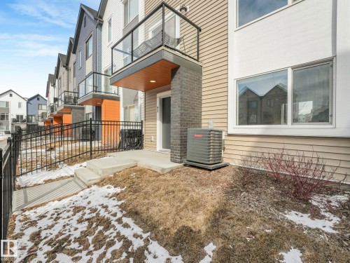 The property features modern exterior siding in varying tones, a private balcony with glass railing, and a ground-level patio area - 95 1010 Rabbit Hill Road, Edmonton, AB - Outdoor
