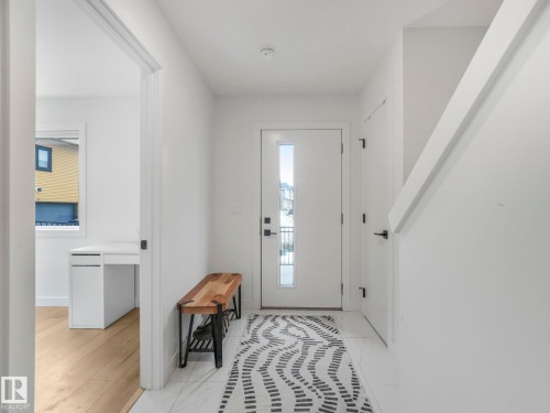 Entryway featuring a white door with vertical window panels, a white staircase, and a doorway leading to a room with wood-style flooring - 95 1010 Rabbit Hill Road, Edmonton, AB - Indoor Photo Showing Other Room