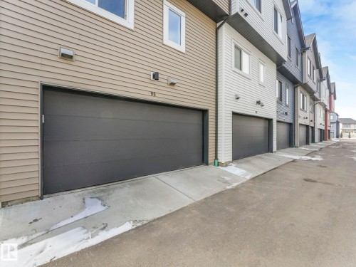The property features a dark gray garage door and beige horizontal siding - 95 1010 Rabbit Hill Road, Edmonton, AB - Outdoor With Exterior