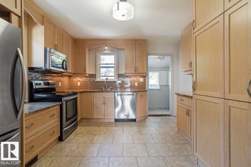 The kitchen features light-toned cabinetry, granite countertops, stainless steel appliances, and a tiled backsplash - 8736 76 Avenue, Edmonton, AB - Indoor Photo Showing Kitchen