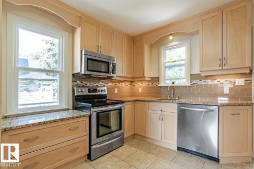 The kitchen features light wood cabinetry, stainless steel appliances, granite countertops, and a tiled backsplash - 8736 76 Avenue, Edmonton, AB - Indoor Photo Showing Kitchen