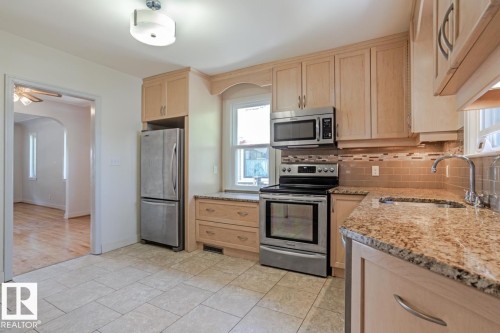 The kitchen features tile flooring, light wood cabinetry, stainless steel appliances, and granite countertops - 8736 76 Avenue, Edmonton, AB - Indoor Photo Showing Kitchen