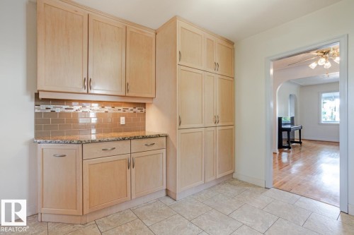 Kitchenette area featuring light wood cabinetry with silver hardware, a granite countertop, and a tiled backsplash - 8736 76 Avenue, Edmonton, AB - Indoor