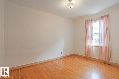 This room features hardwood floors, a window with natural light, and a ceiling-mounted light fixture - 8736 76 Avenue, Edmonton, AB - Indoor Photo Showing Other Room