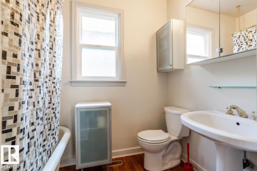 Bathroom featuring a white pedestal sink with brass-toned fixtures, a toilet, a window, and a storage cabinet - 8736 76 Avenue, Edmonton, AB - Indoor Photo Showing Bathroom