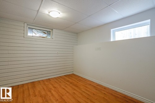 This room features wood-look flooring, white paneled walls, and a dropped ceiling with a flush-mount light fixture - 8736 76 Avenue, Edmonton, AB - Indoor Photo Showing Other Room