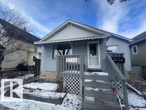 The property features light blue siding, a covered porch, and a gray wooden staircase leading to the entrance - 8736 76 Avenue, Edmonton, AB - Outdoor