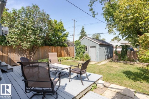 The property features a spacious backyard with a deck, a lawn, and mature trees, offering a private outdoor retreat - 8736 76 Avenue, Edmonton, AB - Outdoor With Deck Patio Veranda