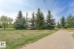 The property is located within a scenic park setting, featuring mature evergreen trees and expansive green spaces - 
