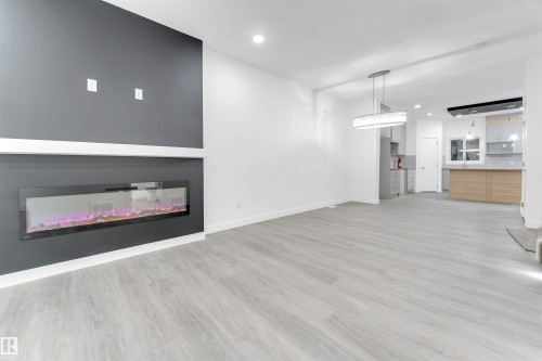 Open concept living area featuring light-toned flooring, a modern electric fireplace with a dark accent wall, and recessed lighting - 444 Crystal Creek Link, Leduc, AB - Indoor With Fireplace