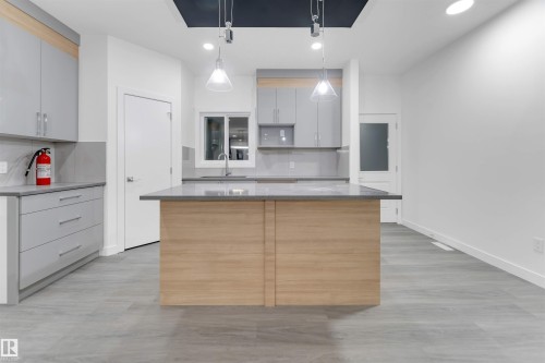 Modern kitchen featuring light gray cabinetry, a central island with a contrasting wood base and a gray countertop, and pendant lighting - 444 Crystal Creek Link, Leduc, AB - Indoor Photo Showing Kitchen
