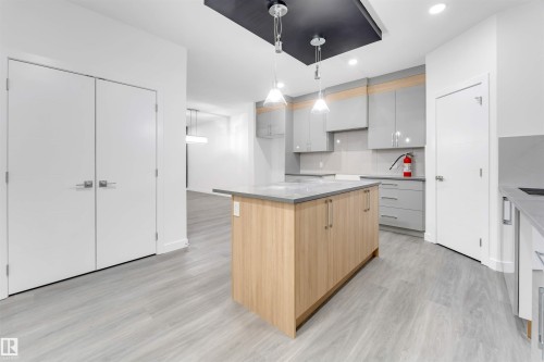 Contemporary kitchen featuring a central island with a light wood finish, grey countertops, and sleek grey cabinetry - 444 Crystal Creek Link, Leduc, AB - Indoor Photo Showing Kitchen