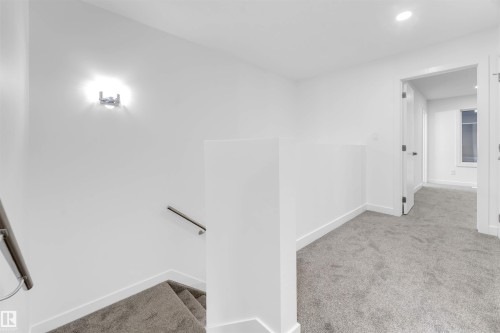 Bright hallway with light gray carpeting and white walls, featuring a modern wall sconce and recessed lighting - 444 Crystal Creek Link, Leduc, AB - Indoor Photo Showing Other Room