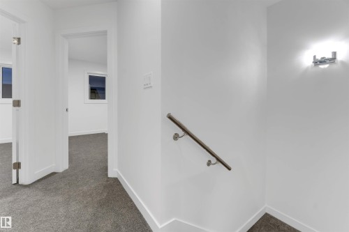 The property features a hallway with gray carpeting and white walls, leading to rooms with windows - 444 Crystal Creek Link, Leduc, AB - Indoor Photo Showing Other Room