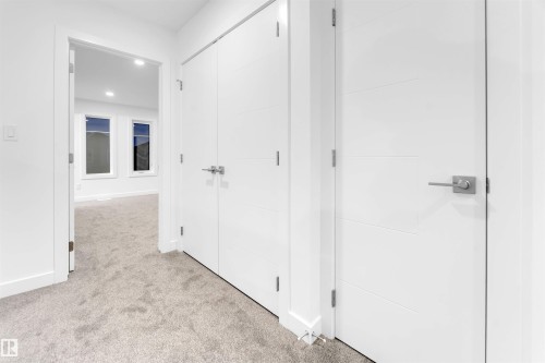 The property features plush carpeted flooring, white walls, and modern white doors with brushed nickel hardware - 444 Crystal Creek Link, Leduc, AB - Indoor Photo Showing Other Room