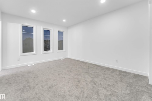 This bright room features three windows providing natural light, recessed ceiling lights, and light gray carpet - 444 Crystal Creek Link, Leduc, AB - Indoor Photo Showing Other Room