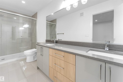 Contemporary bathroom featuring a dual vanity with light grey and wood-finish cabinetry, a large mirror, and a shower with a sliding glass door - 444 Crystal Creek Link, Leduc, AB - Indoor Photo Showing Bathroom