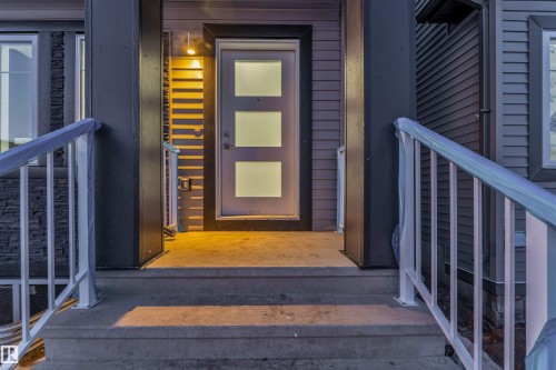 The property features a concrete front entry with steps and railings, a modern front door with three frosted glass panels, and exterior lighting illuminating the entrance - 444 Crystal Creek Link, Leduc, AB - Outdoor With Exterior