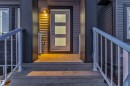 The property features a concrete front entry with steps and railings, a modern front door with three frosted glass panels, and exterior lighting illuminating the entrance - 444 Crystal Creek Link, Leduc, AB  - Outdoor With Exterior 