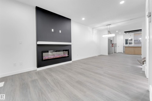 This open concept interior features light wood-look flooring, a modern linear fireplace with a dark accent wall, and a view into the kitchen area - 444 Crystal Creek Link, Leduc, AB - Indoor Photo Showing Living Room With Fireplace