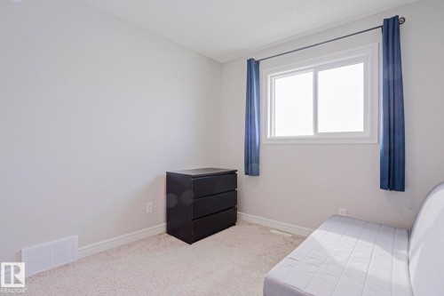 This room features light-colored walls and carpeting, a window with blue curtains, and white trim - 1424 Mcconachie Boulevard, Edmonton, AB - Indoor Photo Showing Bedroom