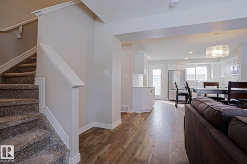 The property features an open-concept living space with wood-style flooring, a kitchen with white cabinetry and stainless steel appliances, and a carpeted staircase - 1424 Mcconachie Boulevard, Edmonton, AB - Indoor Photo Showing Other Room