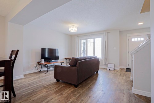 Living area featuring light wood-style flooring, a window with white curtains, and a white front door with windowpanes - 1424 Mcconachie Boulevard, Edmonton, AB - Indoor Photo Showing Living Room