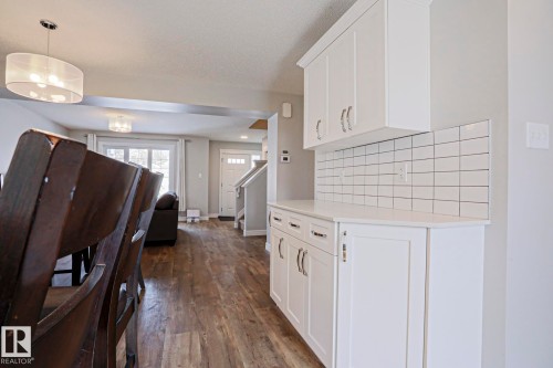 This open-concept interior features wood-look flooring and white cabinetry with coordinating white subway tile backsplash - 1424 Mcconachie Boulevard, Edmonton, AB - Indoor