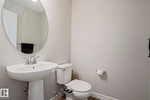 Bathroom with a pedestal sink, a toilet, and a circular mirror - 1424 Mcconachie Boulevard, Edmonton, AB - Indoor Photo Showing Bathroom