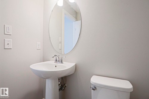 Bathroom featuring an oval mirror, a pedestal sink with a chrome faucet, and a toilet - 1424 Mcconachie Boulevard, Edmonton, AB - Indoor Photo Showing Bathroom