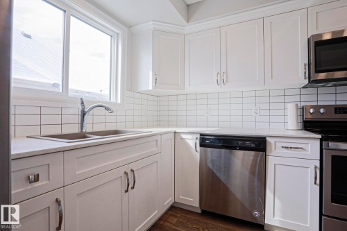 The kitchen features white cabinetry, white countertops, a white tile backsplash, a stainless steel sink, and stainless steel appliances including a dishwasher, microwave, and range - 1424 Mcconachie Boulevard, Edmonton, AB - Indoor Photo Showing Kitchen With Stainless Steel Kitchen With Double Sink With Upgraded Kitchen