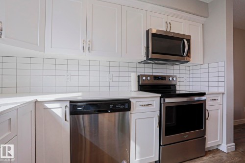 The kitchen showcases white cabinetry with chrome hardware, a subway tile backsplash, and stainless steel appliances including a microwave, range, and dishwasher - 1424 Mcconachie Boulevard, Edmonton, AB - Indoor Photo Showing Kitchen
