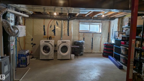 The property features a laundry area with two front-loading machines, a window with blinds, and exposed ceiling joists - 1424 Mcconachie Boulevard, Edmonton, AB - Indoor Photo Showing Basement