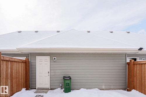 The property features a peaked roof, light-colored siding, and a white door, set within a fenced area - 1424 Mcconachie Boulevard, Edmonton, AB - Outdoor With Exterior