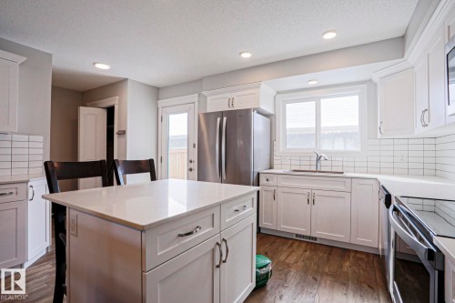 The kitchen features an island with a light-colored countertop, white cabinetry with silver hardware, a stainless steel refrigerator, and a window above the sink - 1424 Mcconachie Boulevard, Edmonton, AB - Indoor Photo Showing Kitchen With Stainless Steel Kitchen With Upgraded Kitchen