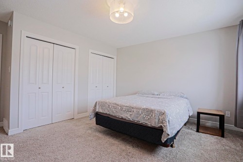 The property features a room with light-colored carpeting, two white bi-fold closets, and a ceiling light fixture - 1424 Mcconachie Boulevard, Edmonton, AB - Indoor Photo Showing Bedroom