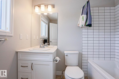 This bathroom features a white vanity with a countertop and an integrated sink, illuminated by a light fixture above a wall-mounted mirror - 1424 Mcconachie Boulevard, Edmonton, AB - Indoor Photo Showing Bathroom