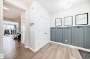 The entryway features light-toned wood flooring, a white trim, and a decorative paneled wall in a charcoal grey with black coat hooks - 2935 Chokecherry Common, Edmonton, AB  - Indoor Photo Showing Other Room 