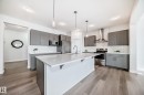 The kitchen features a spacious island with a white countertop, grey cabinetry, stainless steel appliances, and wood-style flooring - 2935 Chokecherry Common, Edmonton, AB  - Indoor Photo Showing Kitchen With Upgraded Kitchen 