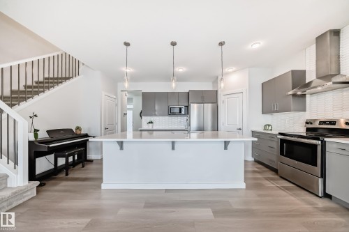 Contemporary kitchen featuring a spacious island with a light-colored countertop, stainless steel appliances, and sleek grey cabinetry - 2935 Chokecherry Common, Edmonton, AB - Indoor Photo Showing Kitchen With Upgraded Kitchen