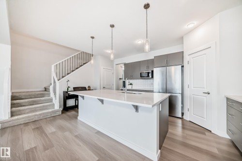 Open concept living space featuring a contemporary kitchen island with a white countertop and pendant lighting, stainless steel appliances, and wood-look flooring - 2935 Chokecherry Common, Edmonton, AB - Indoor Photo Showing Kitchen With Upgraded Kitchen