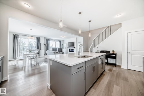 The kitchen features a spacious island with a sink, grey cabinetry, and pendant lighting - 2935 Chokecherry Common, Edmonton, AB - Indoor Photo Showing Kitchen With Double Sink With Upgraded Kitchen