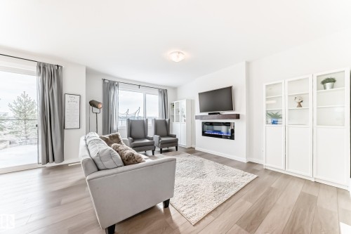 Living area featuring light wood flooring, a fireplace with a mounted television above, and glass-front display cabinets - 2935 Chokecherry Common, Edmonton, AB - Indoor Photo Showing Living Room With Fireplace